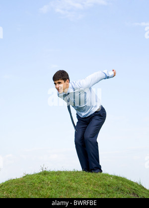 Handsome businessman standing on green grass and going to leap with blue sky at background Stock Photo