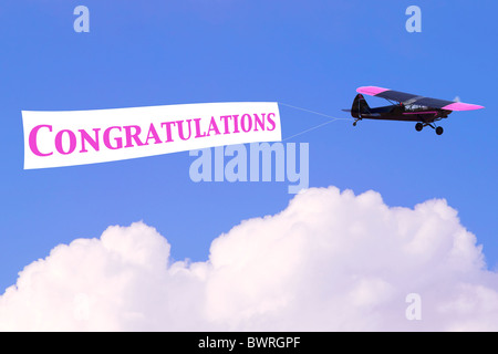 An airplane towing a banner with the word Congratulations in pink, good for female related themes or birth of a baby girl Stock Photo