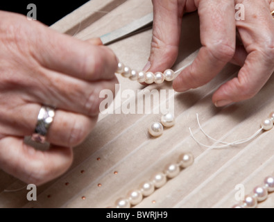 Close hand jeweler stringing pearls on a necklace Stock Photo