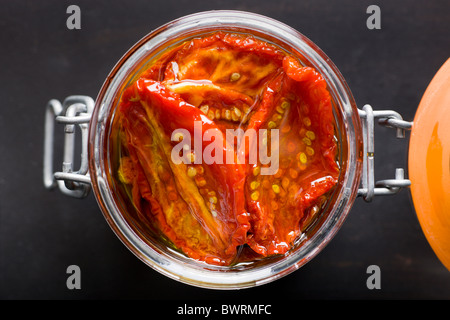 A glass jar filled with Sun-Dried Tomatoes and Olive Oil on a black background. Stock Photo