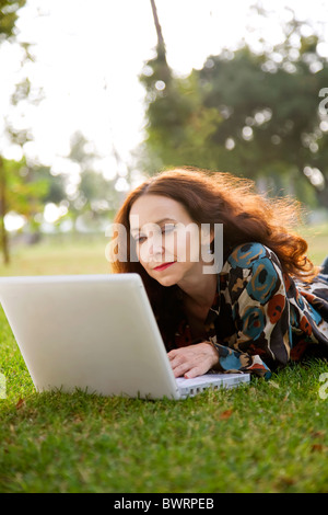 woman, wearing a hearing aid, working on her laptop in a park. Stock Photo