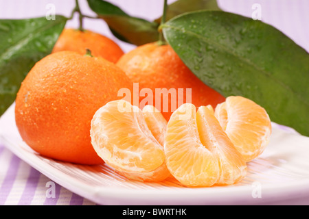 Whole and sectioned clementines over a white dish. Studio shot. Selective focus, extra-shallow DOF. Stock Photo