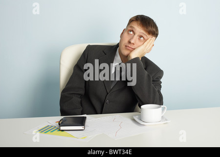 The businessman pensively looks upwards sitting at a table Stock Photo