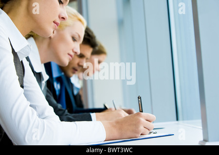 Photo of pretty businesswoman making notes on background of her colleagues at briefing Stock Photo