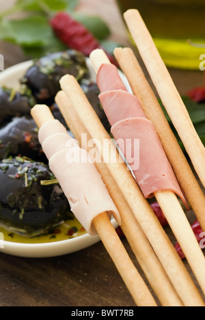 Grissini with ham and pickled black olive ar closeup on wood Stock Photo