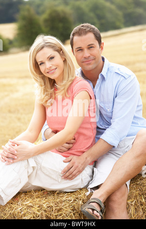 Couple Sitting On Straw Bales In Harvested Field Stock Photo