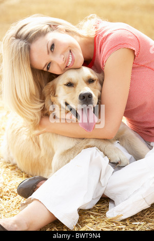Woman Sitting With Dog On Straw Bales In Harvested Field Stock Photo