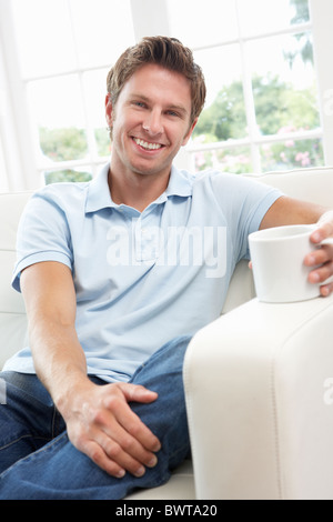 Man Sitting On Sofa Drinking Coffee Relaxing At Home Stock Photo