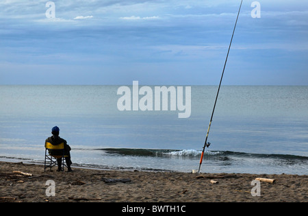 Fisherman sitting on a yellow chair beside his long fishing rod on the beach of Parco Naturale della Maremma,Tuscany, Italy Stock Photo