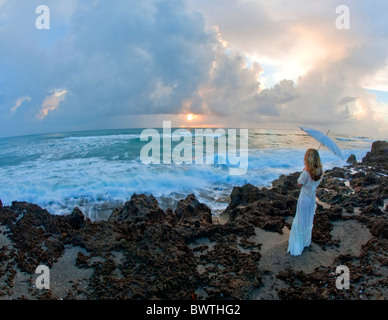 Young woman holding umbrella standing on rocks near ocean Stock Photo