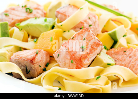 Wild salmon pieces with tagliatelle, mango and avocado as closeup on a white plate Stock Photo