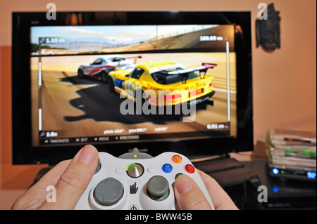 Hands holding controller in front of television screen showing cars in racing game Stock Photo
