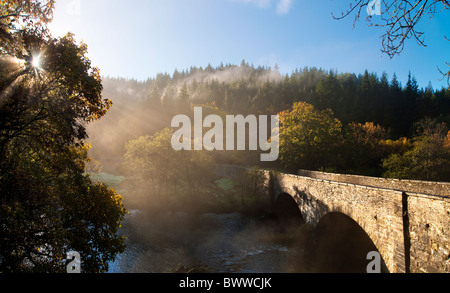 Bridge over The Afon Llugwy on the A5 between Betws y Coed and Capel Curig, North Wales. Sun through trees and rising mist Stock Photo