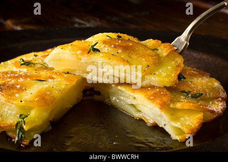 Potato Galettes or Anna garnished with fresh thyme, salt and pepper and served on a rustic plate.