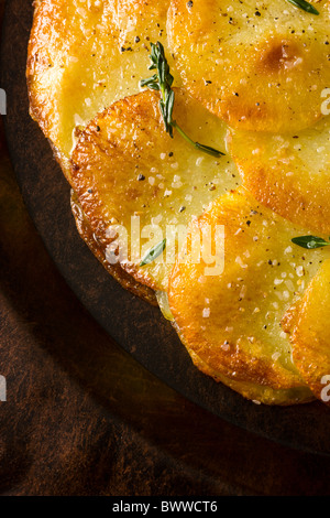 Potato Galettes or Anna garnished with fresh thyme, salt and pepper and served on a rustic plate.