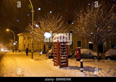 Red telephone and post box in the snow. Snow flakes illuminated by flash. Stock Photo