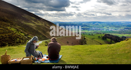 Couple share a picnic on Offas Dyke path with view of the market town Ruthin and the Vale of Clwyd. North Wales UK Stock Photo