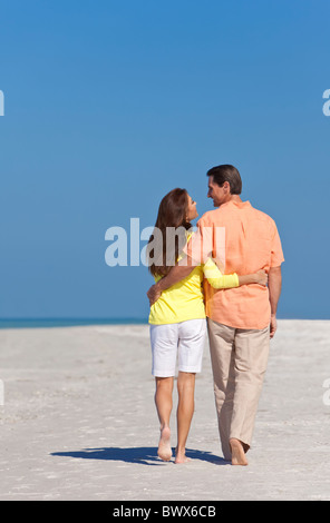 Happy man and woman couple having romantic walk on a deserted beach with bright clear blue sky Stock Photo