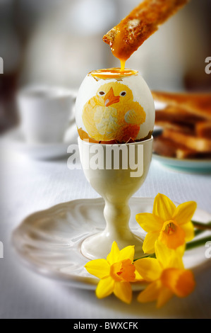 Traditional hand painted decorated boiled easter chic egg in a breakfast setting with toast being dipped into the egg Stock Photo