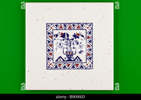 Blue and white pattered square ceramic tile on a green background Stock Photo