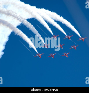 Red arrows hawks display team in arrow formation from upper left to lower right barrel roll trailing smoke - blue sky background Stock Photo