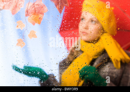 Image of raindrops on window with female under umbrella behind it Stock Photo