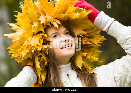 Portrait of smiling young woman touching wreath of maple leaves Stock Photo