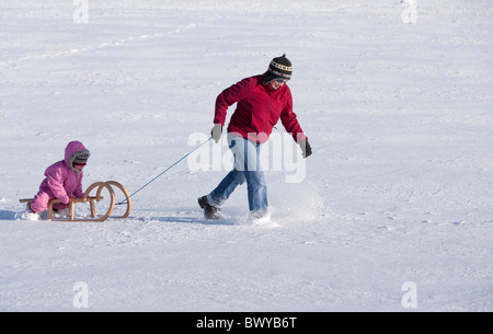 Woman pulling infant girl on wooden sled in winter landscape, Dobel, Black Forest, Gerrmany Stock Photo
