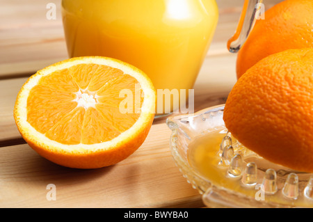 A jug of orange juice with whole and cut oranges and an orange squeezer on a wooden table. Stock Photo