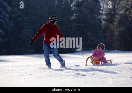 Woman pulling infant girl on wooden sled in winter landscape, Dobel, Black Forest, Germany Stock Photo