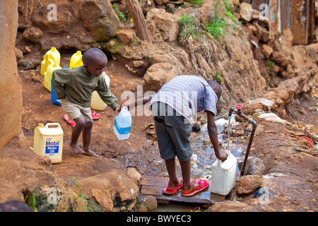 Boys filling containers with water from a tap in the Kibera slums, Nairobi, Kenya Stock Photo