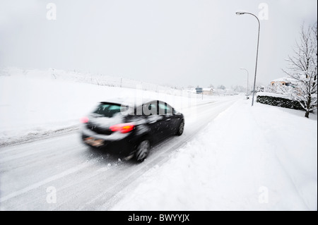 A car drives down a snow-covered road in a Swiss town. Motion blur on the car. Stock Photo