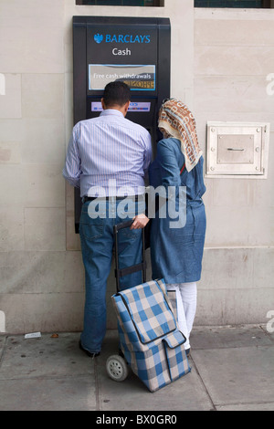 Muslim married couple using a cash machine at  Barclays Bank ATM automated teller machine in London's St John Wood.DAVID MANSELL Stock Photo