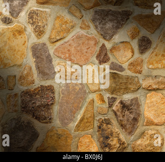 Masonry wall with irregular shaped stones dramatically lit diagonally Stock Photo