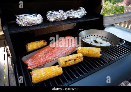 Barbecue in backyard with salmon onions, bakers and corn Stock Photo