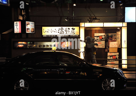 Two workers passing a restaurant at night, Tokyo, Japan Stock Photo