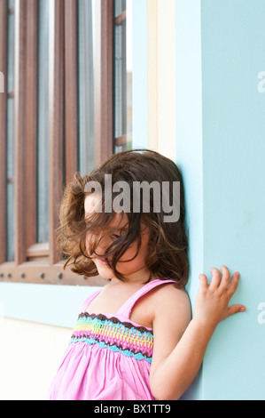 Sad little girl leaning against the wall outside her home Stock Photo
