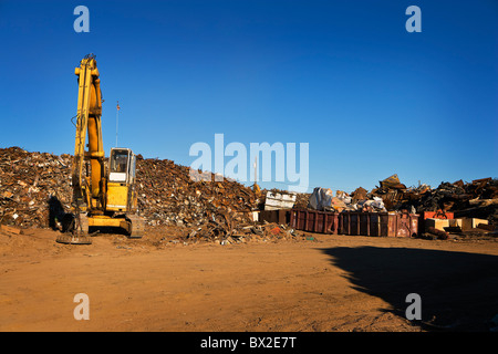 A large yellow crane works with a huge pile of scrap metal, getting it ready for recycling under clear blue skies. Stock Photo