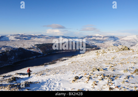 Walker descending Helvellyn lower man in winter in the English Lake District. Thirlmere and Skiddaw in the background Stock Photo