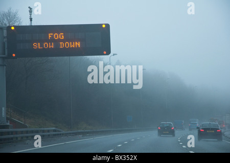 'Fog Slow Down' - motorway warning sign.  Drivers viewpoint with cars and poor visibility.  M5, UK. Stock Photo