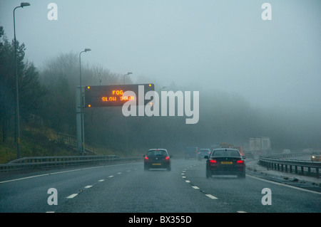 'Fog Slow Down' - motorway warning sign.  Drivers viewpoint with cars and poor visibility.  M5, UK. Stock Photo