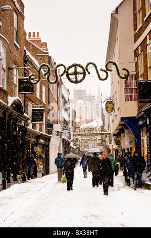 People wearing warm winter clothes walking along Stonegate in the snow. York. Stock Photo