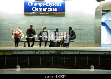 People sitting on bench, using mobile phone, waiting for the train in subway station Champs Elysees Clemenceau in Paris, France Stock Photo