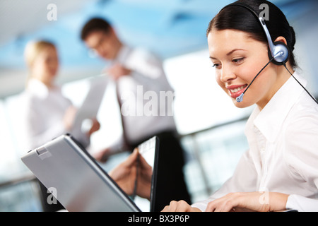 Portrait of executive female in headset working on background of communicating partners Stock Photo