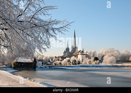 Lichfield Cathedral from Stowe Pool with boat house and tree in winter snow ice and sunshine and hoar frost and blue sky Stock Photo