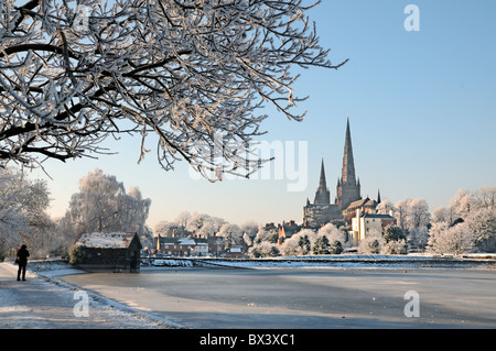 Lichfield Cathedral from Stowe Pool with boat house and tree in winter snow ice and sunshine and hoar frost and blue sky Stock Photo