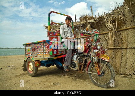 Young man sitting astride a motorcycle tri-rickshaw in a small fishing village on the Island of Diu, India Stock Photo
