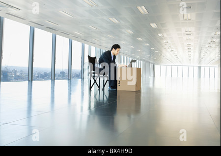 Businessman working on laptop in empty office space using cardboard box as desk Stock Photo