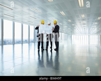 Three executives in hardhats looking at plans in empty office space Stock Photo