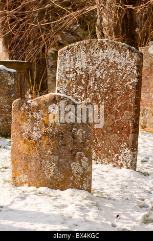Ancient gravestones in winter snow at the churchyard of St James Church in the Cotswold village of Chipping Campden. England. Stock Photo
